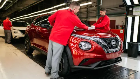 Workers in red shirts and grey trousers work on hybrid Juke sports utility vehicles on the production line at the Nissan's factory in Sunderland, UK, on Friday, 24 November, 2023.