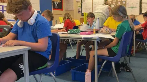 Pupils are seen at their desks with their feet in blue plastic boxes of cold water.