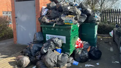 BBC Black bin bags of rubbish on the floor and overflowing out of industrial bins