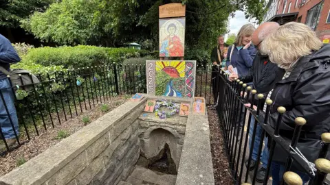 A dressed well with volunteers leaning over railings nearby