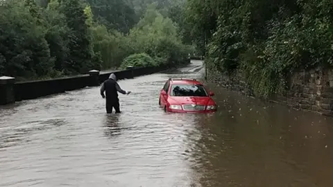 Mark Horrocks Man wades through water as car stuck in flooded road