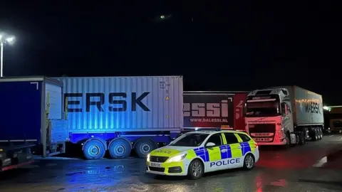 Cambridgeshire Constabulary Police car in front of lorries at night