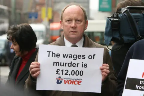 Pacemaker Traditional Unionist Voice leader Jim Allister holds a placard which reads: The wages of murder is £12,000