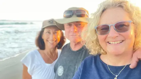 Family photo all three smiling at the camera, on a beach