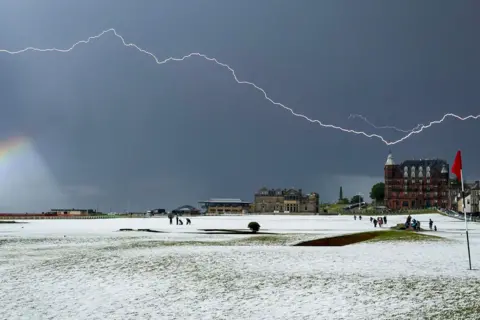 Glen Gardiner A golf course is covered with snow and hail. A flash of lightning illuminates the sky.