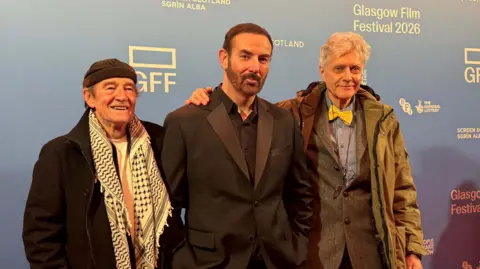 Three men stand in front of a blue background