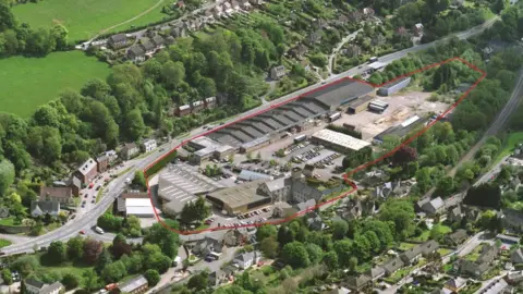 An aerial view of the Brimscombe Port site, an industrial area with large warehouses surrounded by homes and green countryside 