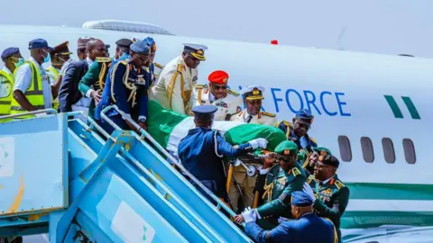 Military men - all in formal dress - carry Muhammadu Buhari's coffin down from an aeroplane.