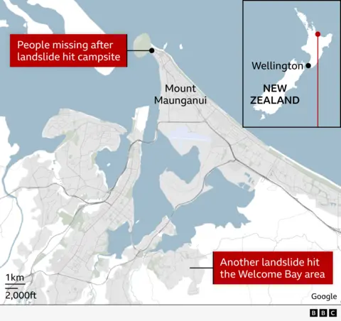 Mappa che mostra l'area del Monte Maunganui nella Bay of Plenty della Nuova Zelanda. Un segnale segnala un campeggio dove mancano persone a causa di una frana. Un'altra area segnalata mostra una seconda frana nella zona di Welcome Bay, a sud. Sono visibili strade, corsi d'acqua e caratteristiche costiere, con una barra di scala che mostra le distanze. Una mappa nel riquadro mostra la Nuova Zelanda con Wellington contrassegnata per il contesto della posizione.