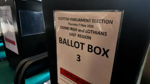 A close-up image of a ballot box. It is a big black box with a white sign saying "Ballot Box 3, Scottish Parliament Election, Thursday 7 May 2026, Edinburgh and Lothians East Region"