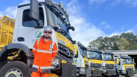 a row of gritter vehicles with Surrey County Council logos and a driver in orange hi-vis standing in front