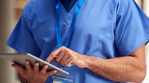 Getty Images A member of health care staff at a hospital looking at notes on a tablet.  