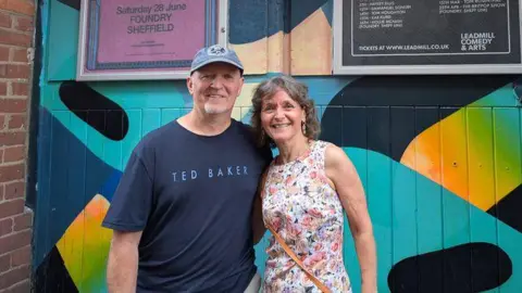 BBC A man and woman stood in front of a painted wooden doorway