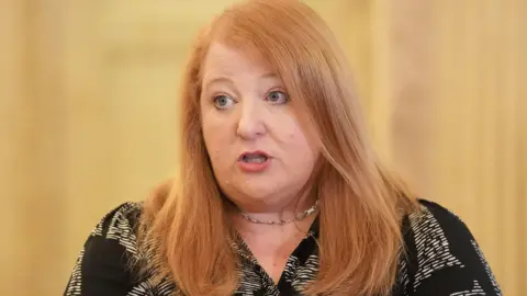PA Media Naomi Long wearing a black and white shirt and necklace. She is speaking. She has red hair.