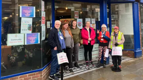 Exterior of the Wycombe Food Hub community shop, showing a group of volunteers standing outside the entrance beneath the organisation’s signage on the High Street.