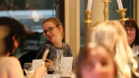 Community Leisure UK Alisha Burley smiles at she sits at a table in a glamorous-looking ballroom, surrounded by fellow guests