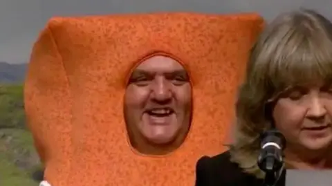 Paul Ellis's smiling face pokes through a fishfinger costume, as the returning officer in the foreground delivers the result. 