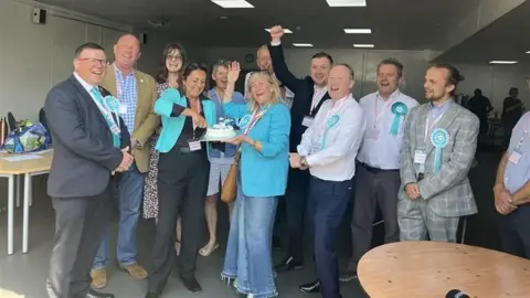 Reform UK councillors and supporters celebrate election victory in Maidstone with a cake.
