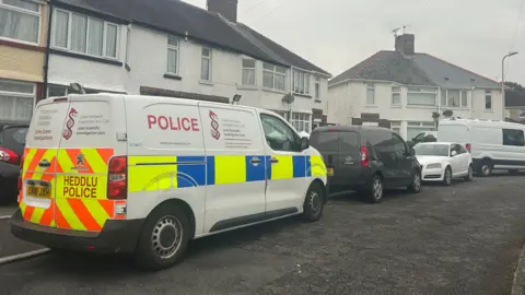BBC A white terraced house with a police van outside