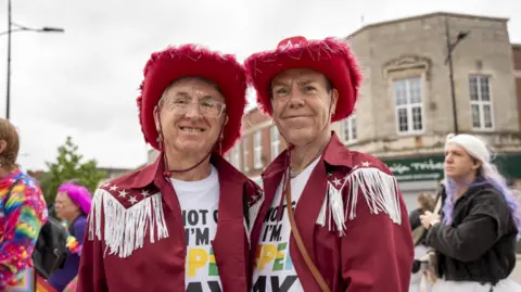 City of Wolverhampton Council Two people in matching red cowboy outfits, with people in colourful clothing behind them
