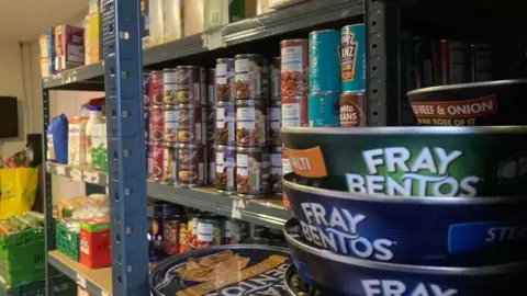 A large array of food cans on shelves and other produce in the background.