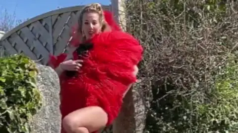 Clare Meardon A woman holding a large red boa in a street.