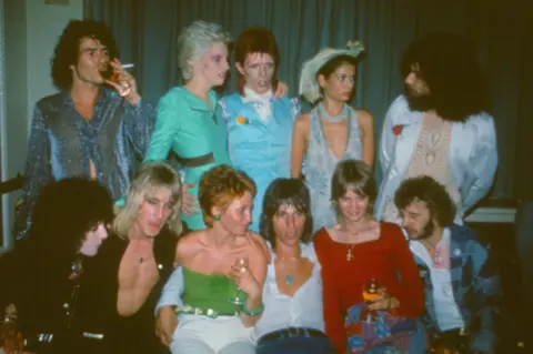 Mark Hayward Archive/Getty Images An archive photo of a group of ten people. Five people are sat at the front with another five stood behind them. they are all dressed in 1970s clothing. Among the group are David Bowie, Lulu, Ringo Starr and Jeff Beck.
