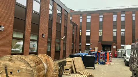 BBC The East Midlands NHS Planned Care Centre, based at the former Brandon Unit at Leicester General Hospital, is pictured. It is a brown brick building with building equipment still outside.