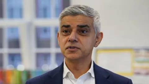 File image of Sadiq Khan, a man with short grey hair wearing a navy blue suit jacket and white shirt, speaking inside a room at a school