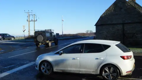 John Rhind A car at a junction with landrover pulling away