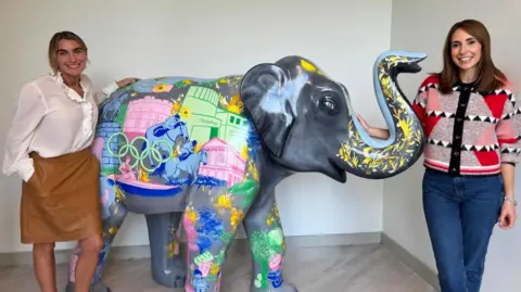 Rachael de Caux on the left and Alex Jones stood next to an elephant, decorated grey and painted with patterns celebrating Berkshire and the Olympics' rings.
