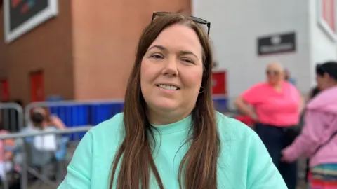 Nicola wears a light blue top and sunglasses perched on her head.