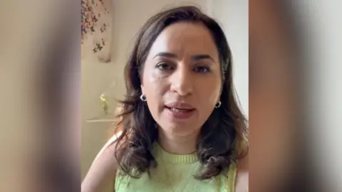Attieh Fard/Facebook Attieh Farad in a grab from one of her campaign videos. She is sitting in a room and has shoulder length brown hair and wears a sleeveless green jersey with a pendant around her neck.