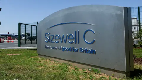 An entrance sign at the Sizewell C construction site in Leiston, Suffolk. It is a grey sign with blue writing that reads: Sizewell C the power of good for Britain.