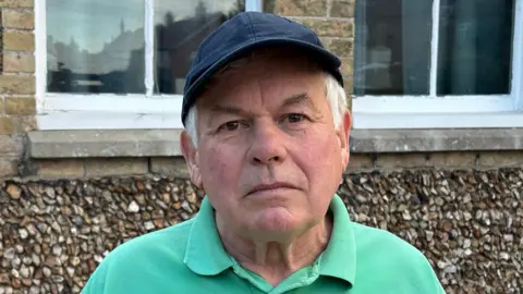 Luke Deal/BBC A head and shoulders image of a man wearing a green polo shirt and a baseball cap. He is looking directly into the camera.