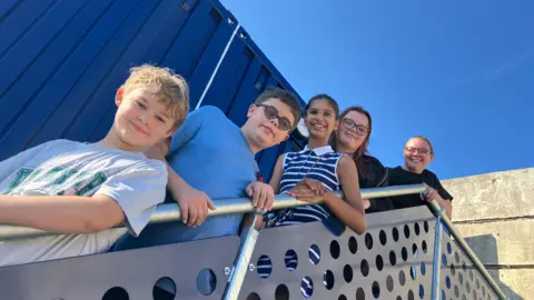 Five young people stand on some stairs in front of a blue shipping container unit.