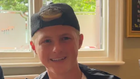 Jack is a young man wearing a black cap backwards. He is smiling and has short, blonde hair. He is sat in a pub.
