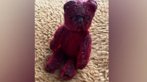 Nicola Christy A tatty red teddy bear sitting on a carpet