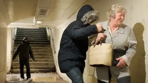 Getty Images A woman's bag is being snatched by two hooded youths in a subway in this generic image of antisocial behaviour.