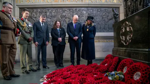 PA Media A number of dignitaries, some in uniform, look down at poppy wreaths at a war memorial