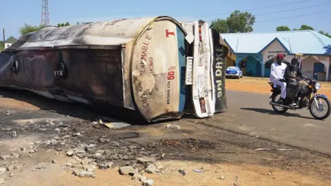 AFP Dua orang mengendarai sepeda motor melewati kapal tanker yang terbakar di pinggir jalan di Majia, Nigeria - 16 Oktober 2024