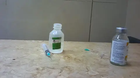 Two bottles sit on a countertop alongside what appears to be a discarded needle and a syringe.