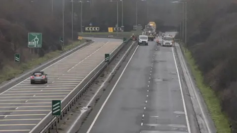 Work being carried out to repair potholes on a dual carriageway. One side of the road is closed as workmen carry out the repairs.
