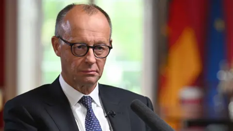 Germany's chancellor sits in a dark jacket and tie 
