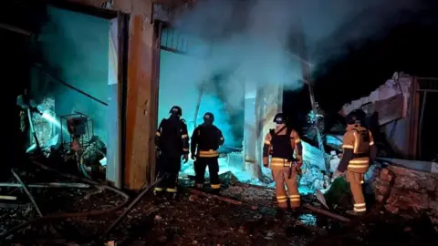 Four people in fire rescue uniforms with torches walk through the rubble of a damaged building in Dnipropetrovsk