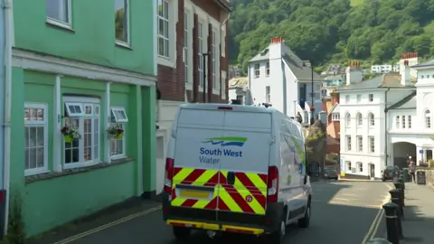 A white van branded with South West Water is driving along a street on a sunny day.