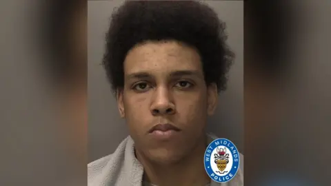 A police mugshot of a young man with Afro-style hair. The West Midlands Police logo has been superimposed in the bottom-right corner.