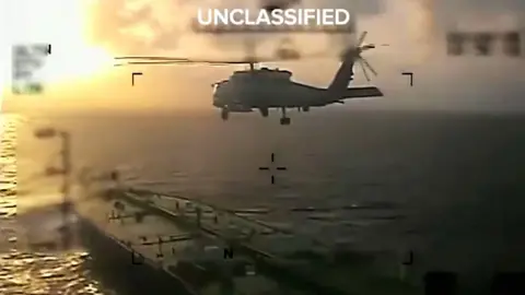 Kristi Noem via X/Reuters A photo released by Kirsti Noem shows a helicopter hovering above a tanker and the word "Unclassified" printed on top. 