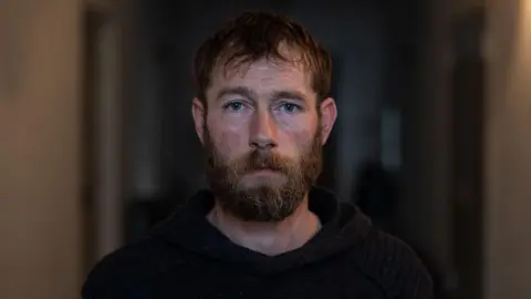 A close up of Chris Garrett a man with ginger hair and a ginger beard, he looks somber