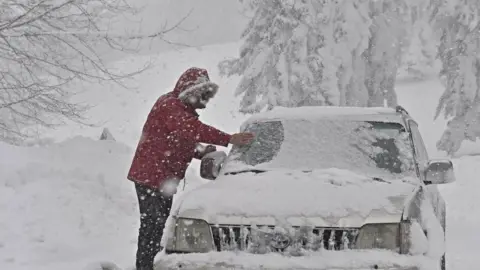 EPA A person clears snow from a vehicle after a heavy snowfall in Casaglia, Mugello, Florence"s province, Italy